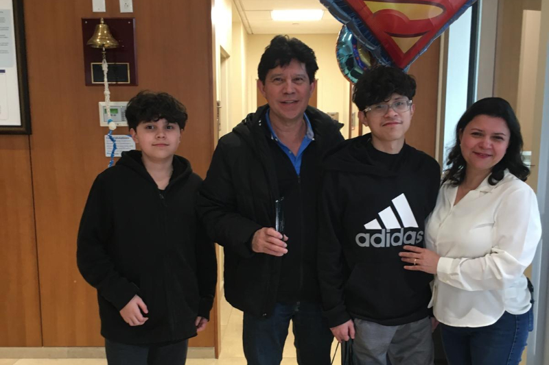 Patient Steven with his family standing and smiling after successful cancer treatment. 