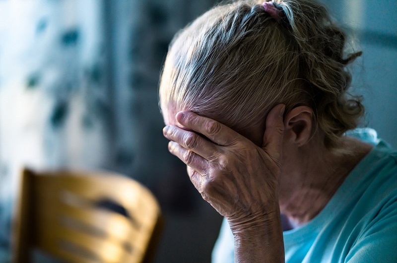 Sad senior woman, with her face in her hands, dealing with loss and grief.