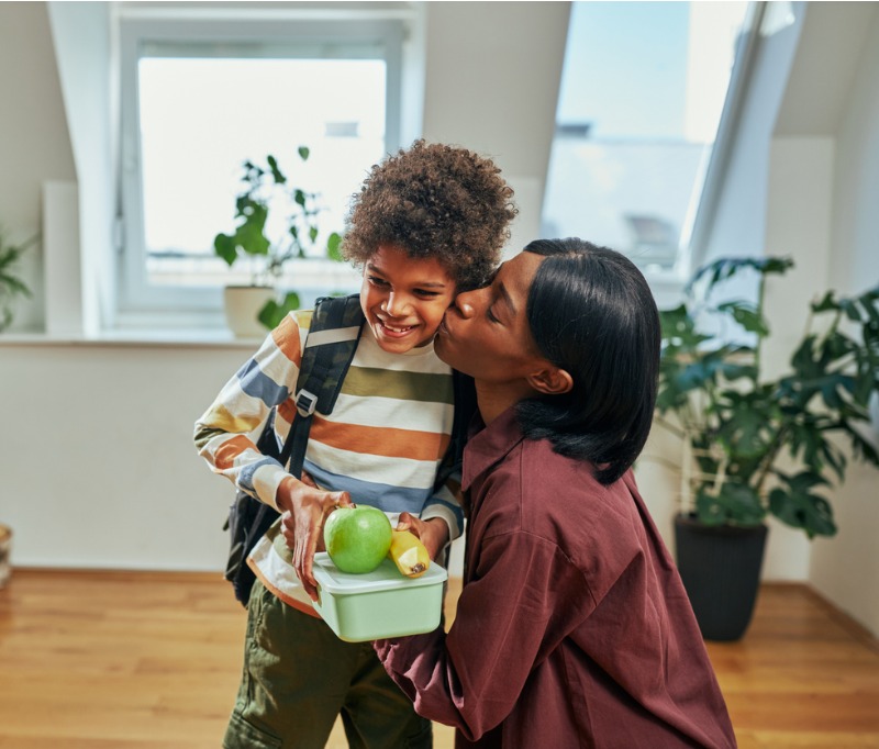 African mother giving lunch box to her schoolboy and kissing him