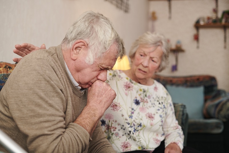 senior man with wife at home coughing badly