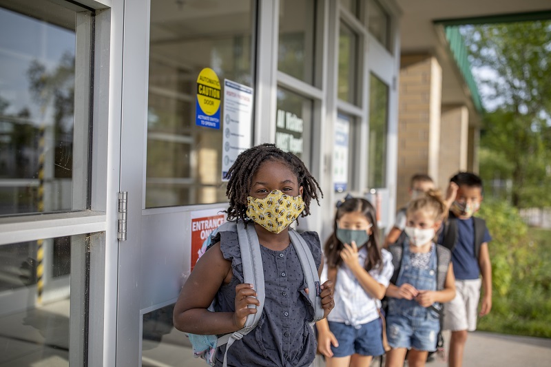 Children waiting in a line outside of their school with masks on.