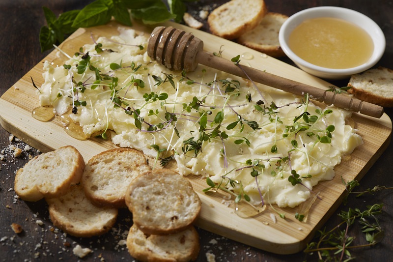 The Viral Butterboard with Fresh Herbs, Micro Greens, Organic Honey and Toasted Baguette Slices on a Bamboo Cutting Board