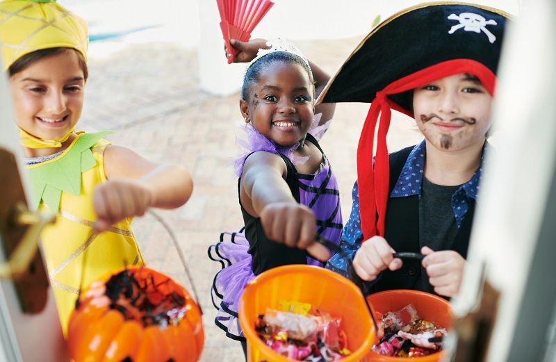 Children dressed up for Halloween at the front door of someone's house, reaching out for candy.