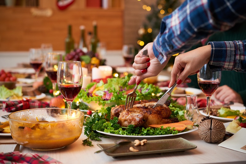 Woman's hands cutting thanksgiving dinner at a table full of food and drinks.
