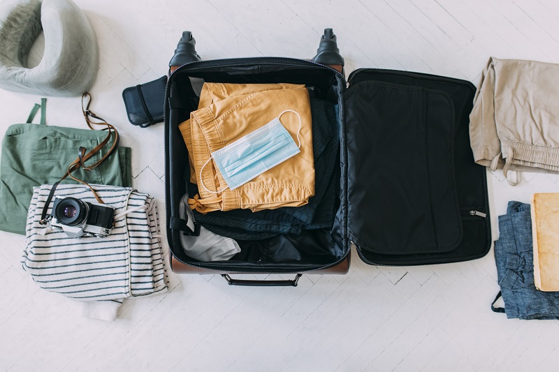 Protective face mask packed into a suitcase along with clothes and a camera. Tips for travel safety.