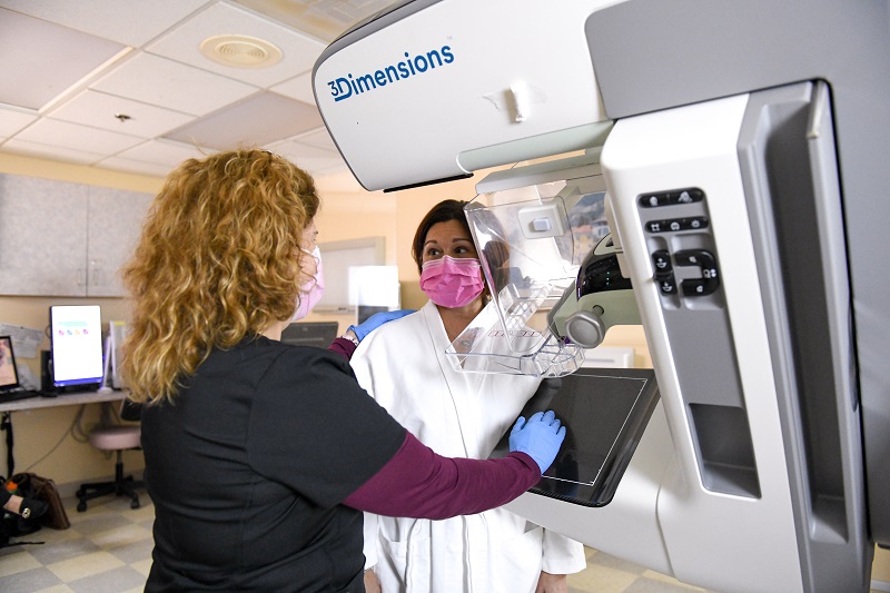 Radiologist helps a patient, in a robe, before a mammogram.