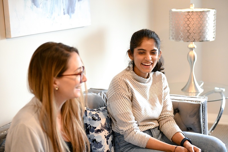 Two friends sitting in the living room smiling and hanging out together.