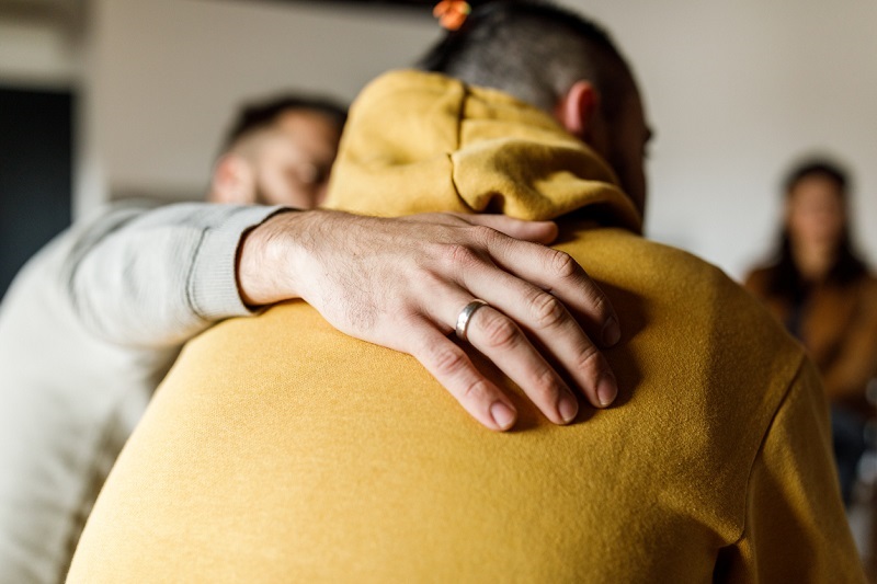 Close up shot of a compassionate man embracing his friend, having an intimate conversation about his mental health and substance use.