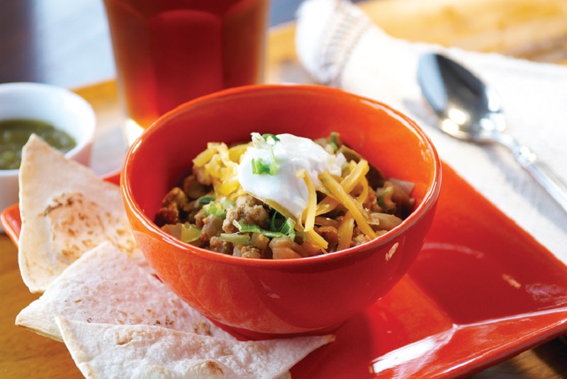 A red bowl of turkey chili - topped with sour cream and shredded cheese.