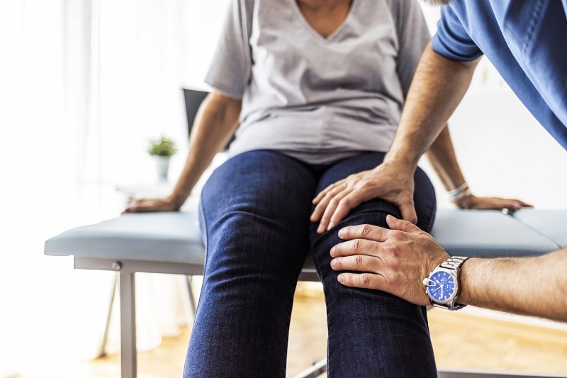 Doctor's hands on a patient's knee, evaluating for osteoarthritis.