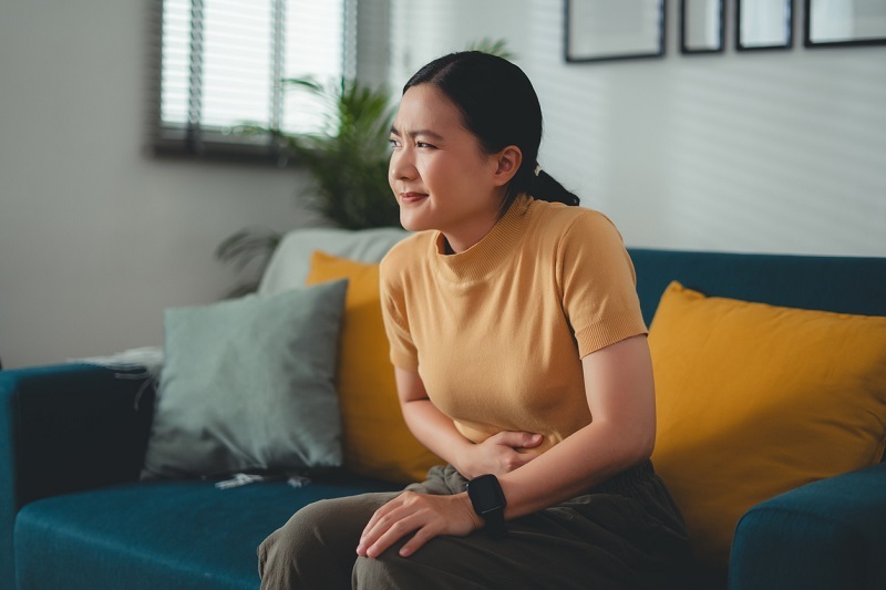 Woman holding her stomach, looking toward the sides, feeling gas pains, holding in a fart.