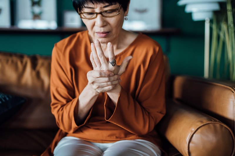 Woman rubbing her hands in discomfort, suffering from arthritis in her hand while sitting on the sofa at home.