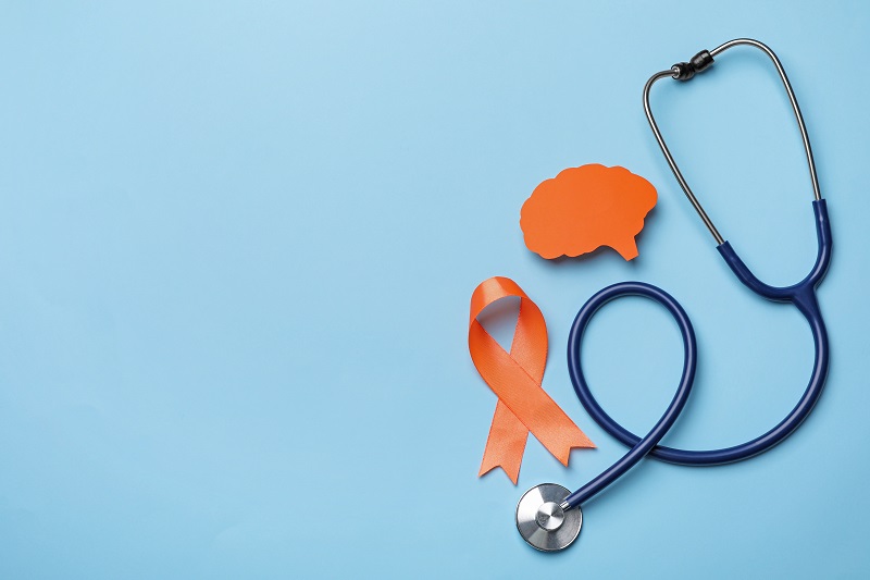 Orange ribbon, stethoscope and paper brain cutout on light blue background. Concept for multiple sclerosis awareness.