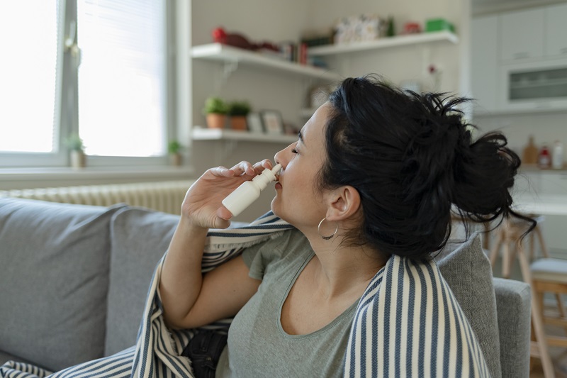 Woman using a nasal spray on the couch, suffering from a migraine.