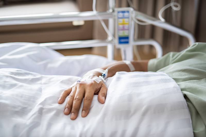 A close-up of a patient's hand with an IV, while in a hospital bed.