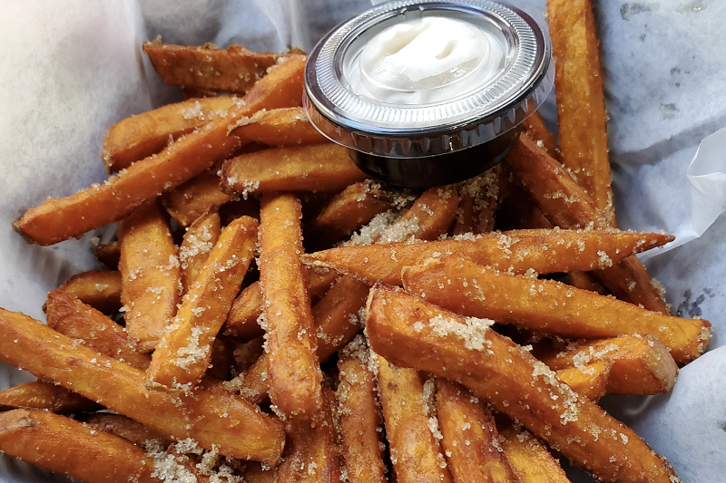 A basket of crisp sweet potato fries with a garlic yogurt dip on the side.