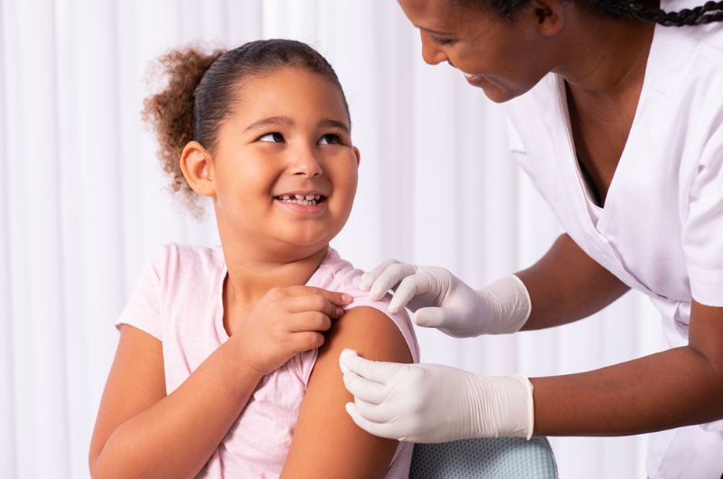 An adolescent girl gets a bandage on her upper arm after a vaccine.