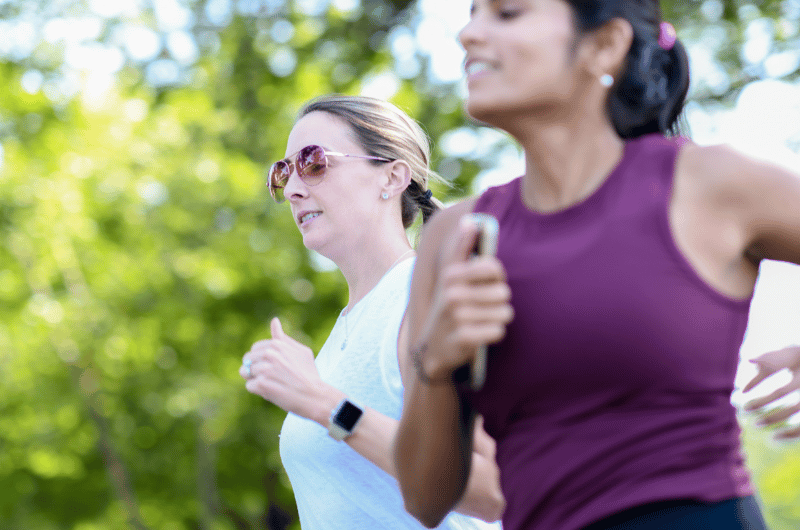 Two young women run outdoors side-by-side.