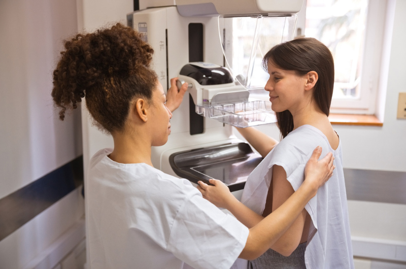 Female doctor talking to young woman during a mammogram in an examination room.
