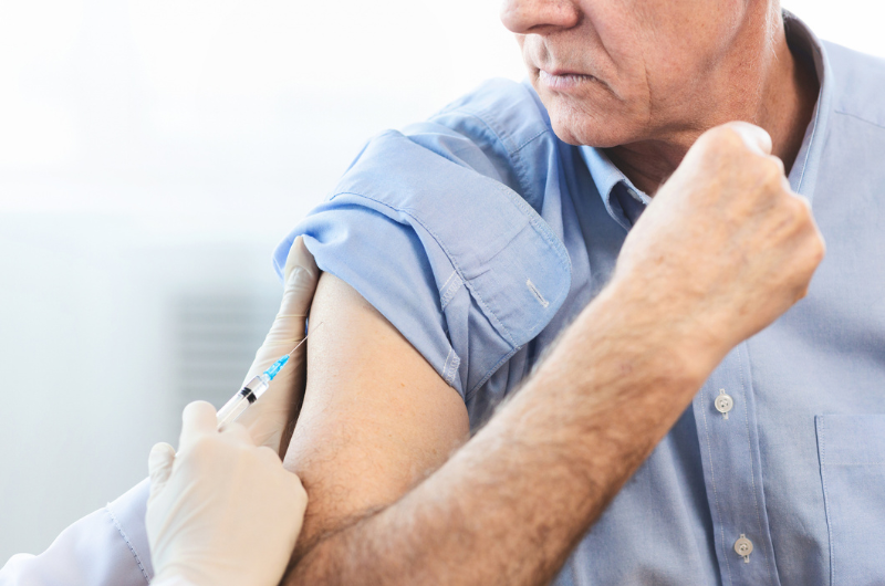 Close-up of unrecognizable doctor doing vaccination for an elderly man.