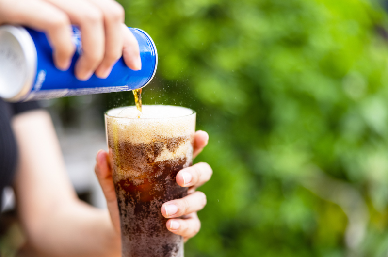 Female hand pouring a diet soda drink from a can to a glass.