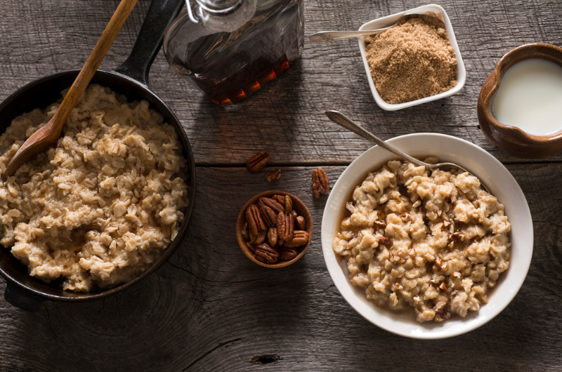 Top-down view of two bowls of oatmeal with side dishes of pecans and brown sugar. 