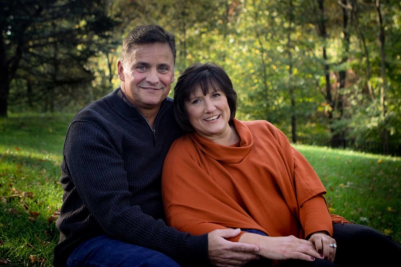 Mike Hennessy and his wife Patti, sitting together hugging and smiling.