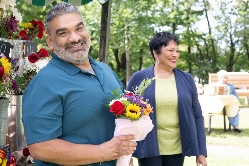 Carlos Mercado holding a bouquet of flowers smiling.