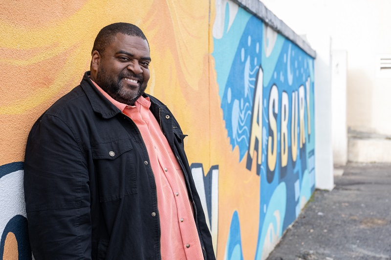 Carin Givens leaning against a colorful wall, smiling.