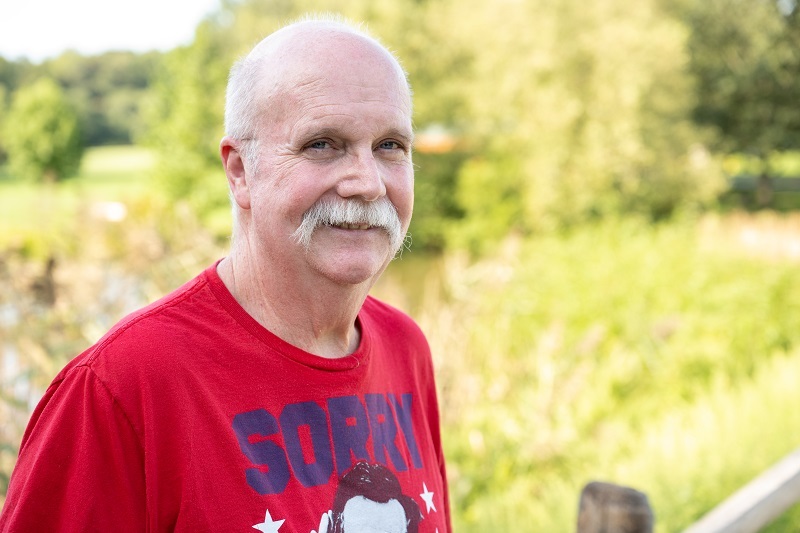 Doug smiling and standing outside in a field park.