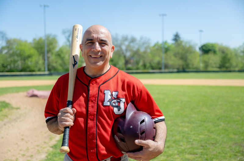 James Morales stands on a baseball field holding a baseball bat and helmet.
