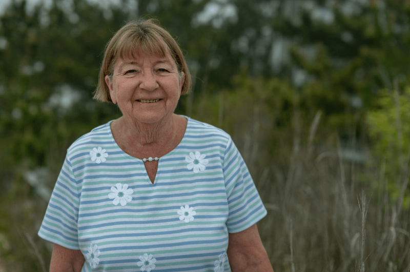 70-year-old retired teacher Martha Groh stands outside and smiles at the camera.