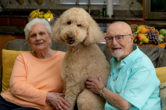 Nick and Barbara sitting on the couch with their golden doodle, Roxie.