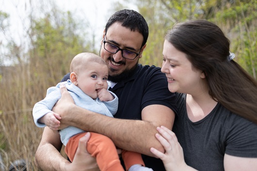 Baby Benny being held by his parents, all smiling, sitting on the couch.